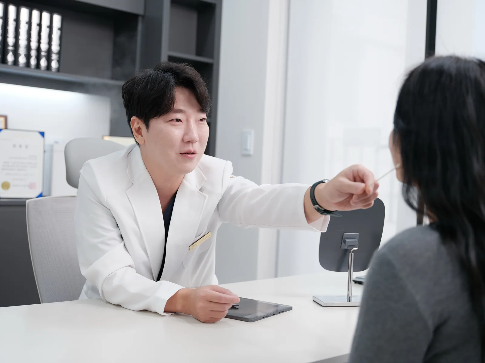 คุณหมอ Jonghwan Choi ชี้จุดบนใบหน้าผู้รับบริการระหว่างการปรึกษาที่ Rewind Plastic Surgery